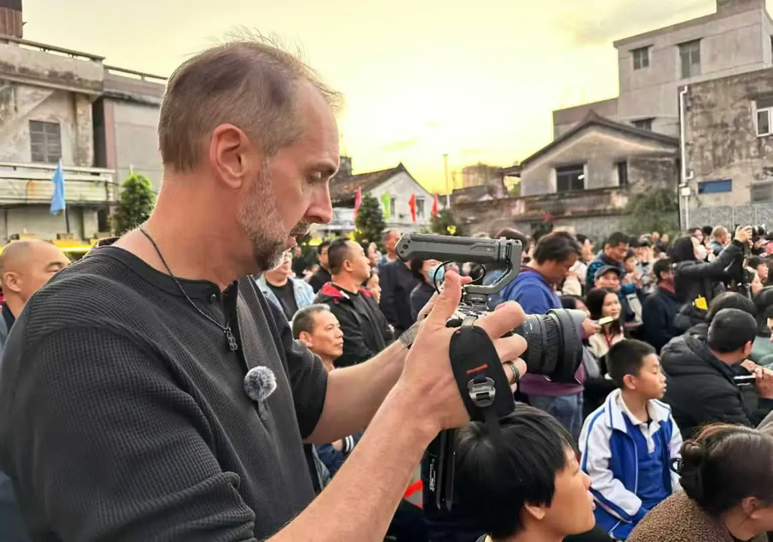 Tim Ramak filming with a handheld camera at a busy outdoor event in Shenzhen